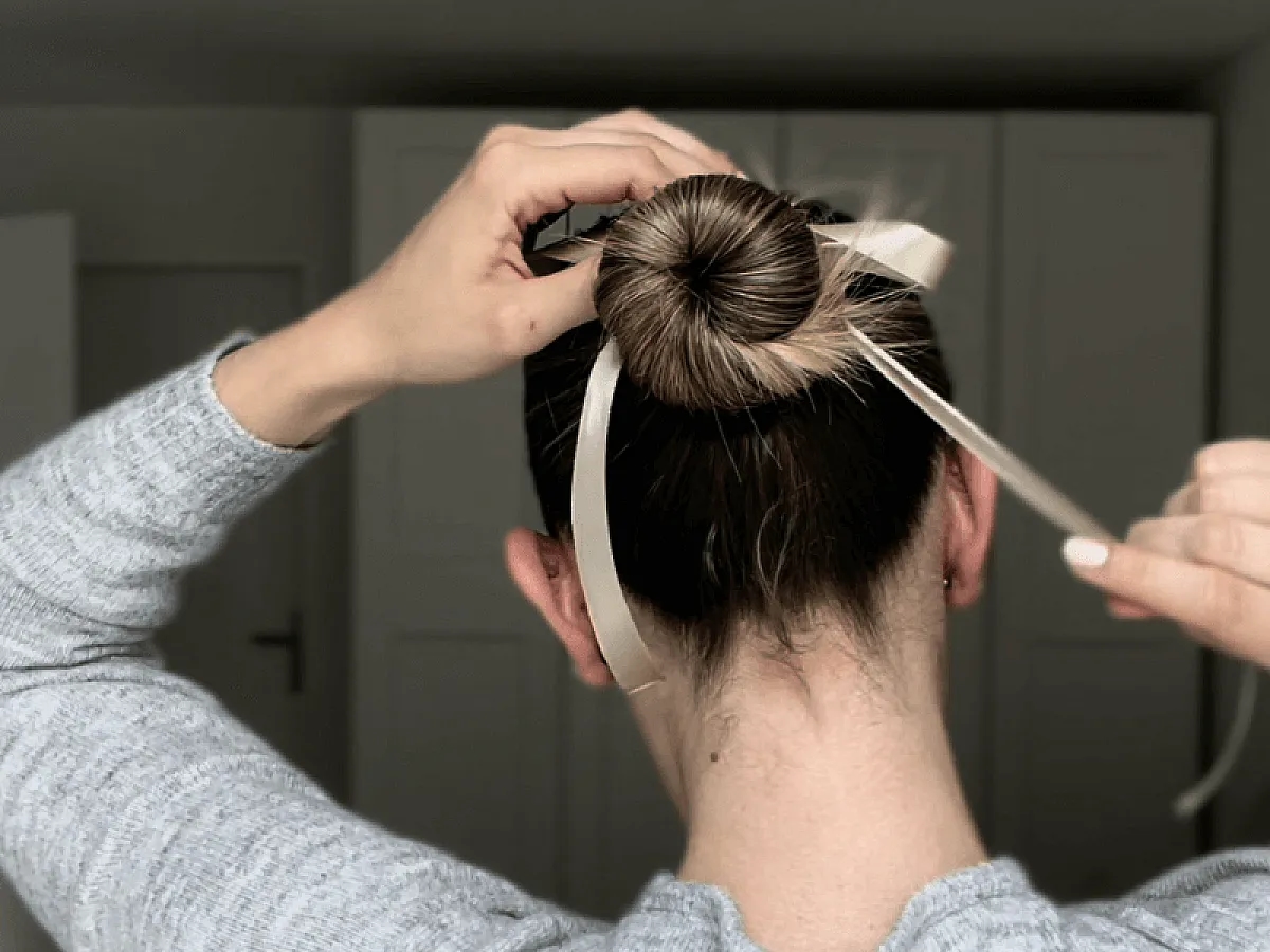 Woman ties a bow around her bun for a trendy ballet core look